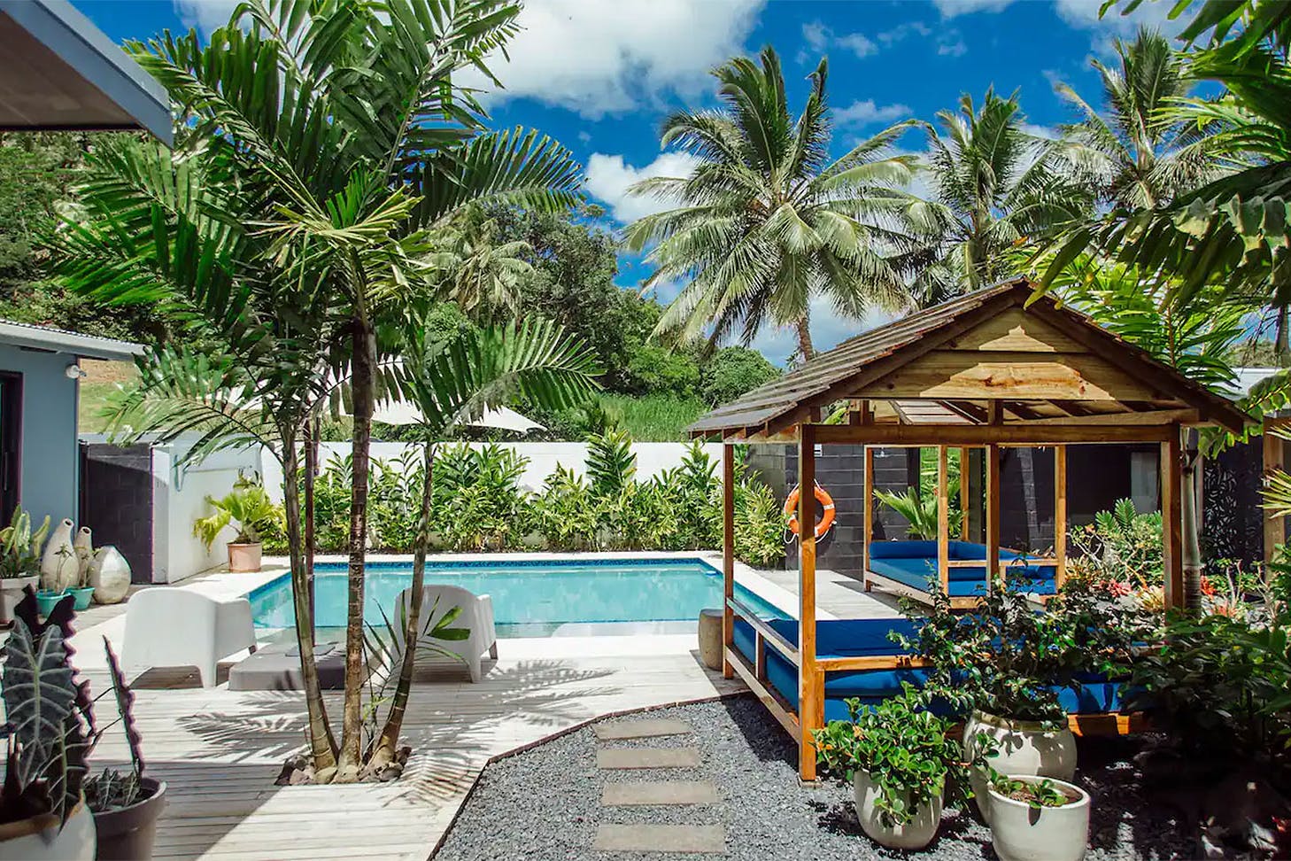 Day beds surround a lush pool amongst greenery in this airbnb in Raro.